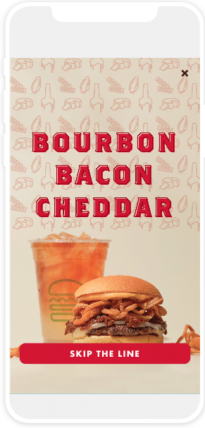 Bourbon Back Cheddar burger advertisement on a smartphone: An image of burger and drink, labeled "Bourbon Bacon Cheddar." A link at the bottom saying: "Skip the line"